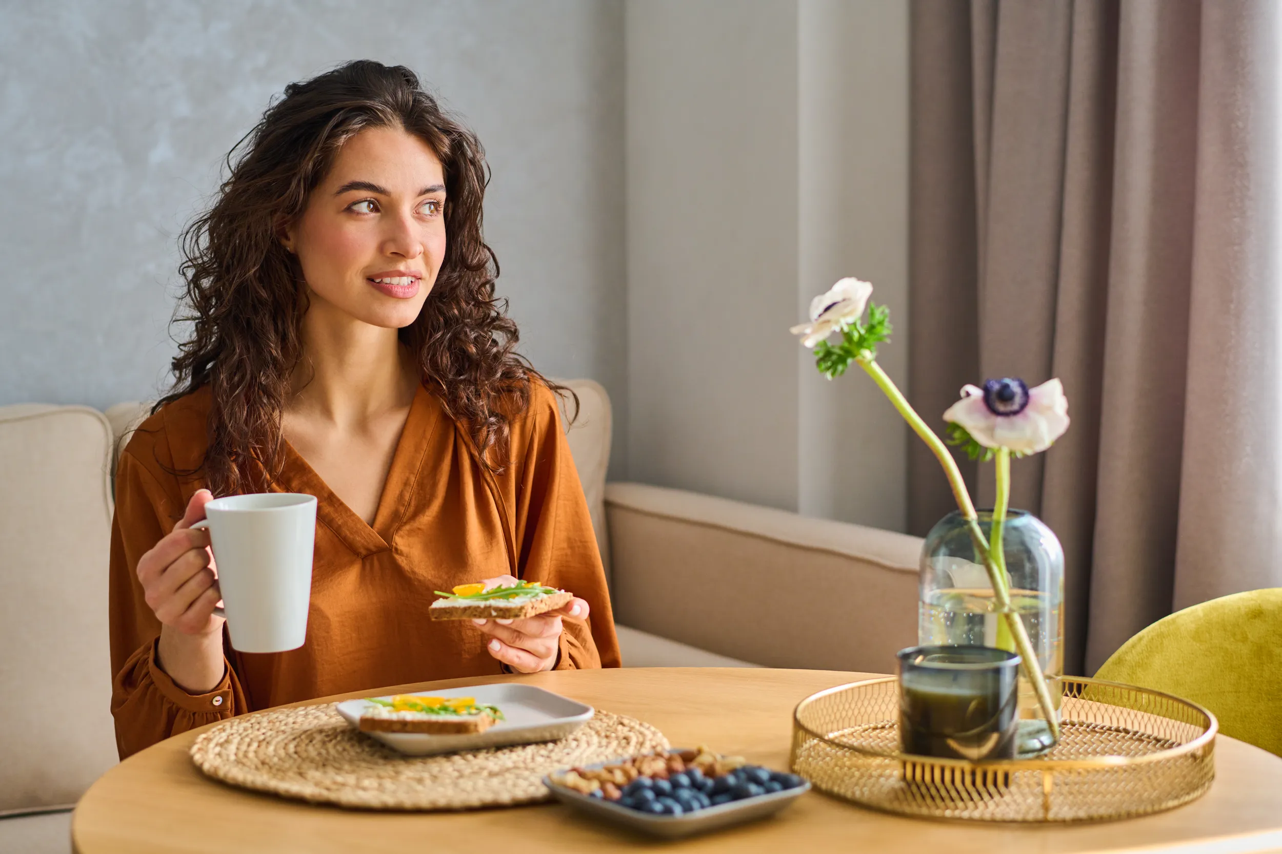 Woman seated at a table eating a simple breakfast in soft morning light.