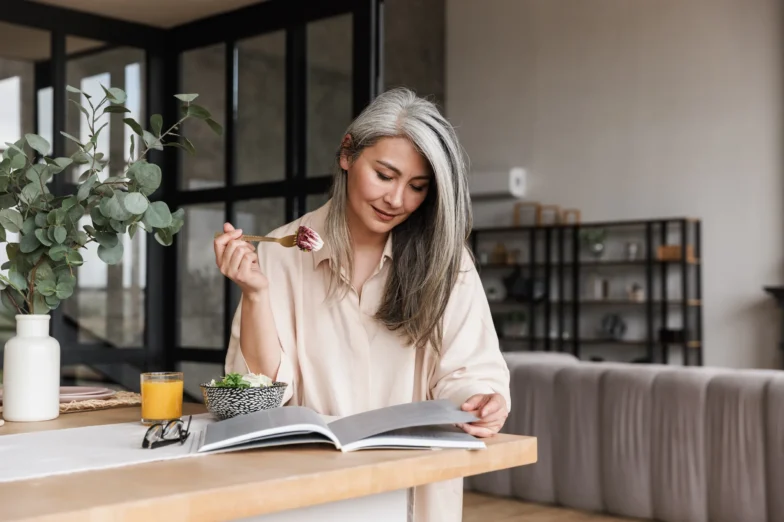 Mature woman eating breakfast while reading, representing cognitive health and healthy aging.