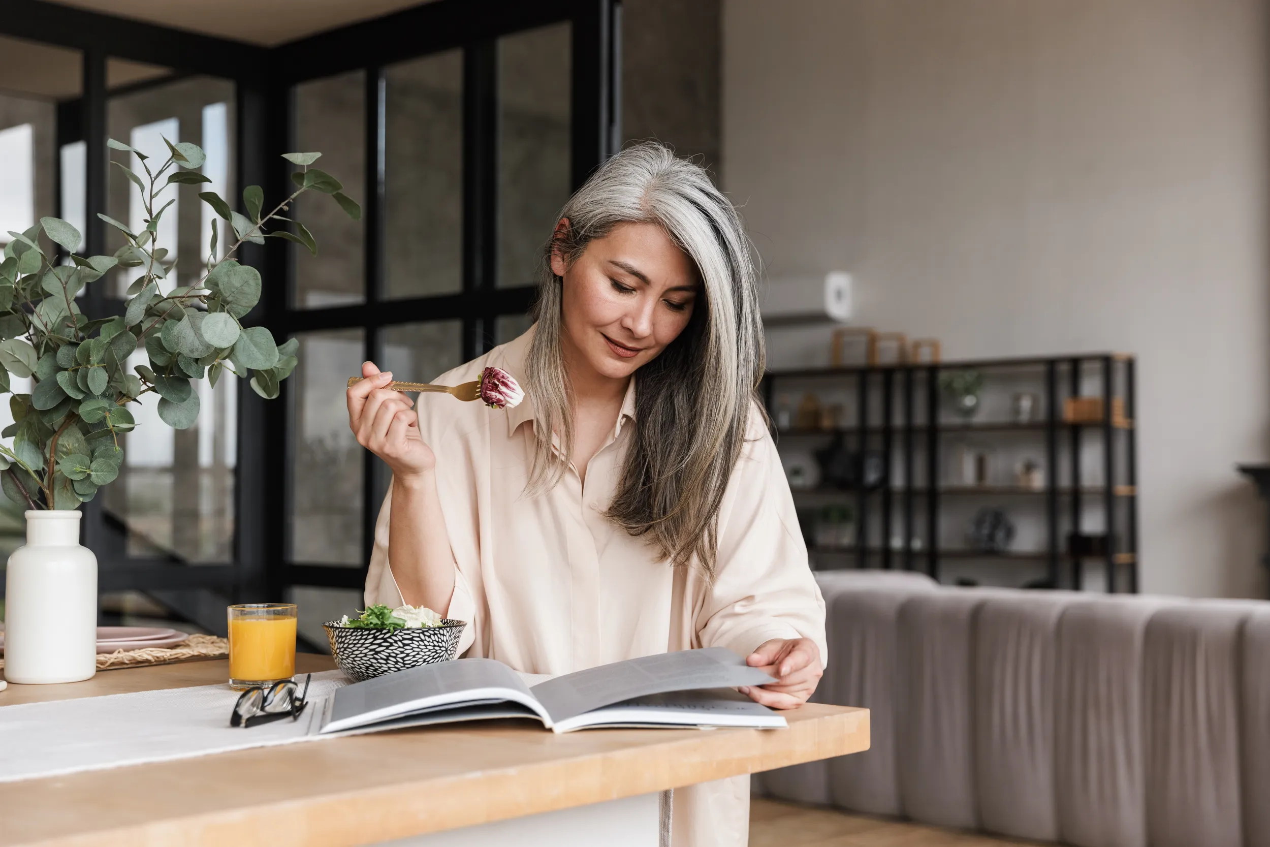 Mature woman eating breakfast while reading, representing cognitive health and healthy aging.
