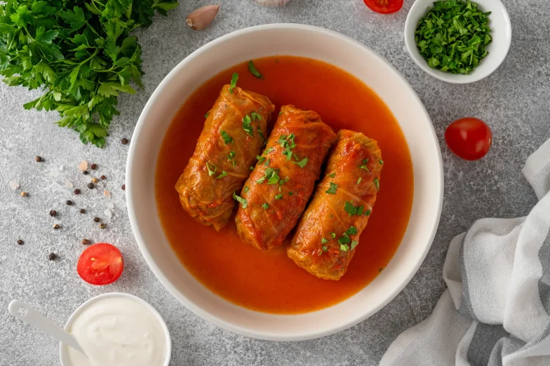 Three stuffed cabbage rolls covered in tomato sauce and garnished with fresh parsley, served in a white bowl.